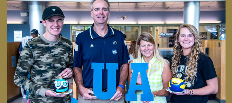Sibling and parents of college student stand with her holding large blue letters that spell UA